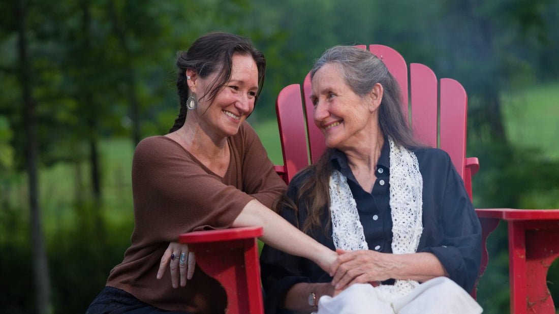 Jess and her mother Barbara smiling at each other in red garden chairs